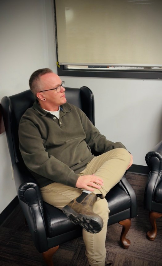 Dean sitting in a chair with one leg crossed over the other